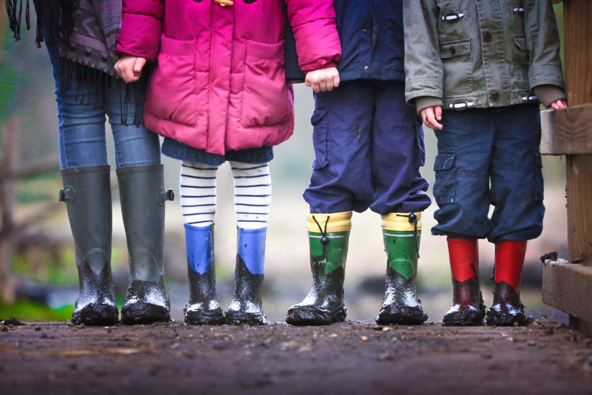 Four children stand wearing bright wellington boots and holding hands